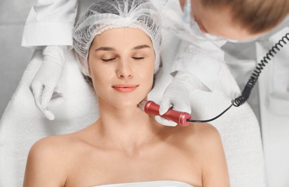 Top view portrait of attractive young woman enjoying procedure cleaning or massage for face. Concept of special procedures for skin with modern professional equipments.